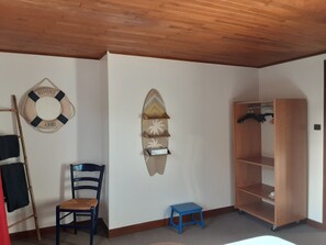 A room with a wooden ceiling, a chair, a small stool, a shelf unit, and a wall-mounted life preserver. - Maison de caractère .La vague douce des Landes (Vielle-Saint-Girons)