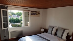 Un dormitorio con cama, ventana, radiador y una mesita de noche pequeña.