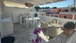Une terrasse sur le toit, dotée d’un espace salon couvert, d’une plante en pot et offrant une vue sur les bâtiments environnants.