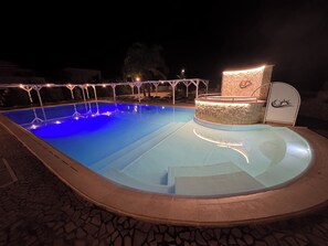 Ein Pool mit Steingestaltung, eine Liegefläche mit Steinwand und ein überdachter Sitzbereich mit einem Logo.
