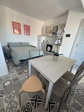 Ein kompakter Wohnraum mit Bett, Esstisch mit Stühlen, Küchenzeile und einer Orchidee im Topf.