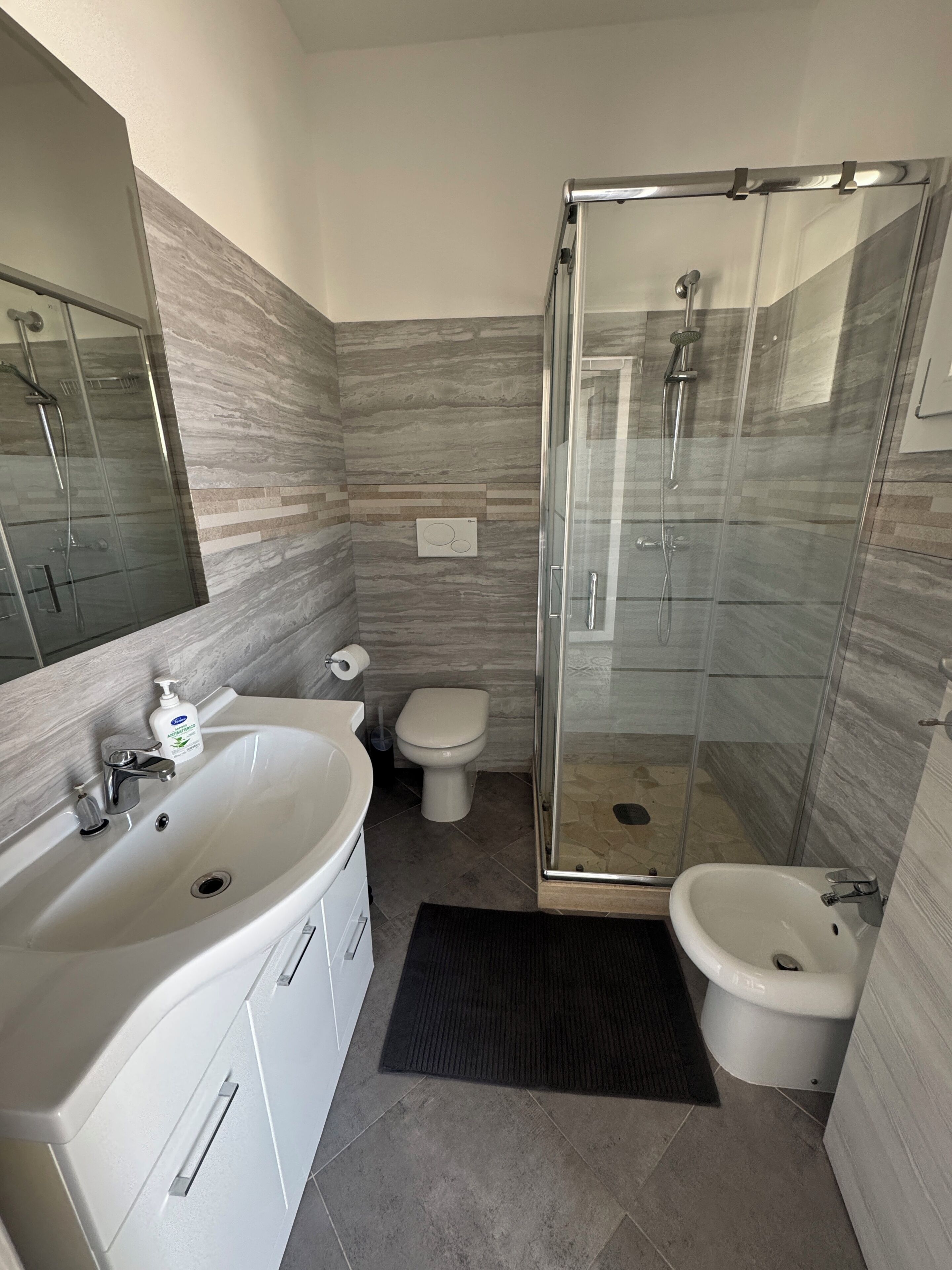 Une salle de bain avec une douche à parois de verre, un lavabo avec un miroir et des toilettes.