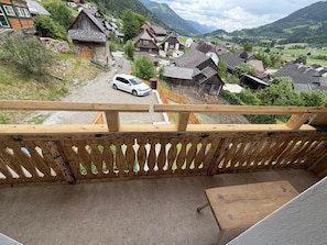 Ein Balkon mit Holzgeländer, der auf ein Dorf mit traditionellen Häusern und einem weißen Auto auf der Straße blickt.