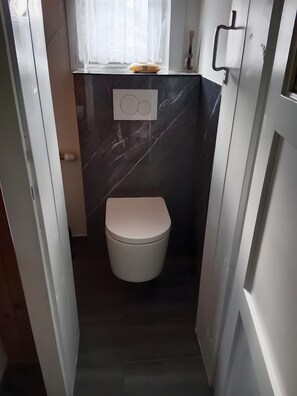 A small, narrow bathroom with a toilet, a window with a curtain, and a wall-mounted air freshener. - Holiday Home 'Ferienhaus Sonnseitn' with Mountain View, Private Terrace and Private Garden (Altlassing)