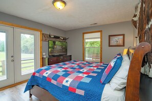 A bedroom with a bed, a television, a wooden headboard, and a window. - 🍃 Quaint Cabin on Cosby Creek 🏞️ Creekside Farm, Hot Tub & Park Access (Cosby)