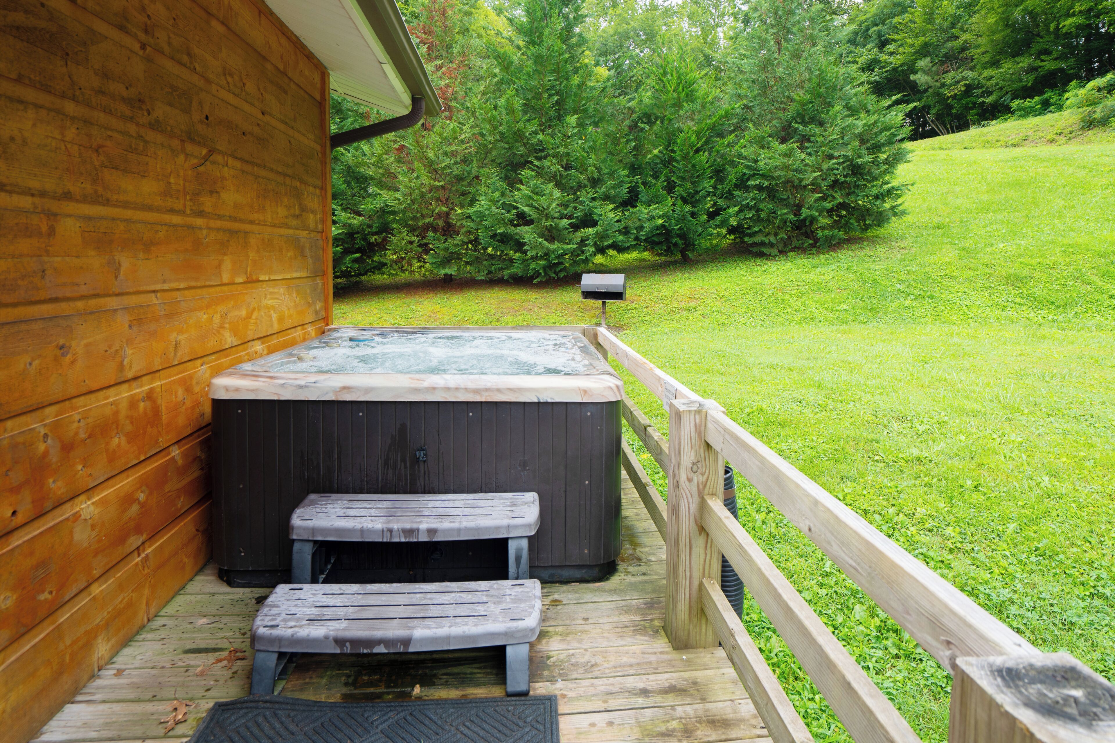 A wooden deck with a hot tub and a bench, surrounded by a wooden fence and lush greenery.