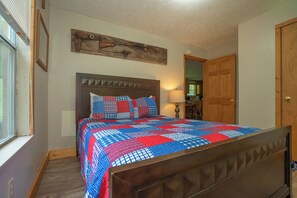 Ein Schlafzimmer mit einem hölzernen Bett, einer gesteppten Decke, einem Holz-Kopfteil, einem Wandbild, einer Tür und einem Fenster.