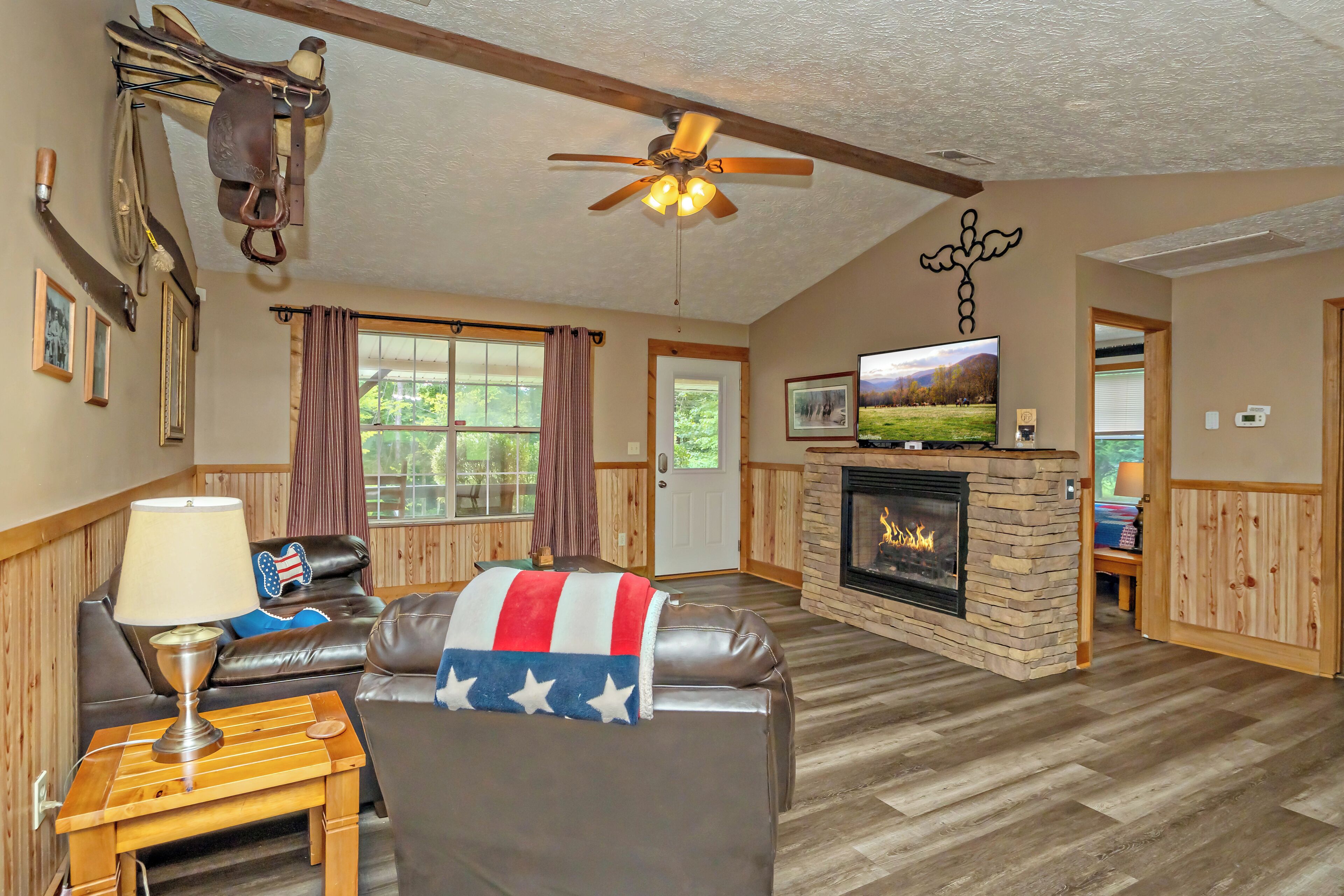 A cozy living room with a fireplace, leather sofas, a wooden coffee table, and a ceiling fan.