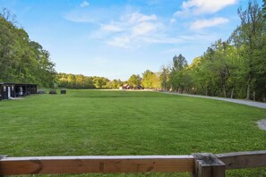 A grassy field with a wooden fence, a building with a red roof, and trees in the background. - 🍃 Quaint Cabin on Cosby Creek 🏞️ Creekside Farm, Hot Tub & Park Access (Cosby)