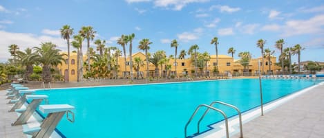 Ein Swimmingpool mit klarem, blauem Wasser, umgeben von Palmen und gelben Gebäuden.