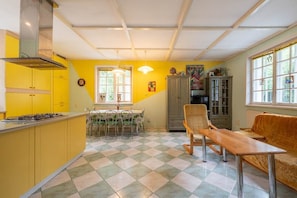 Une cuisine avec des meubles de couleur jaune, une table à manger avec des chaises, un banc en bois et un canapé.