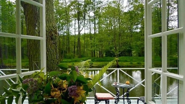 A room with a large window, a table with chairs, and a vase of flowers. - Scenic Riverside House with Beautiful Views (Litwinki)