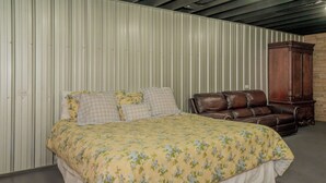 A bedroom with a bed, a leather sofa, and a wooden cabinet. - 🌲 70 Acre Mountain Farmstead 🏞️ Stocked Pond, Game Room & Seclusion (Sevierville)