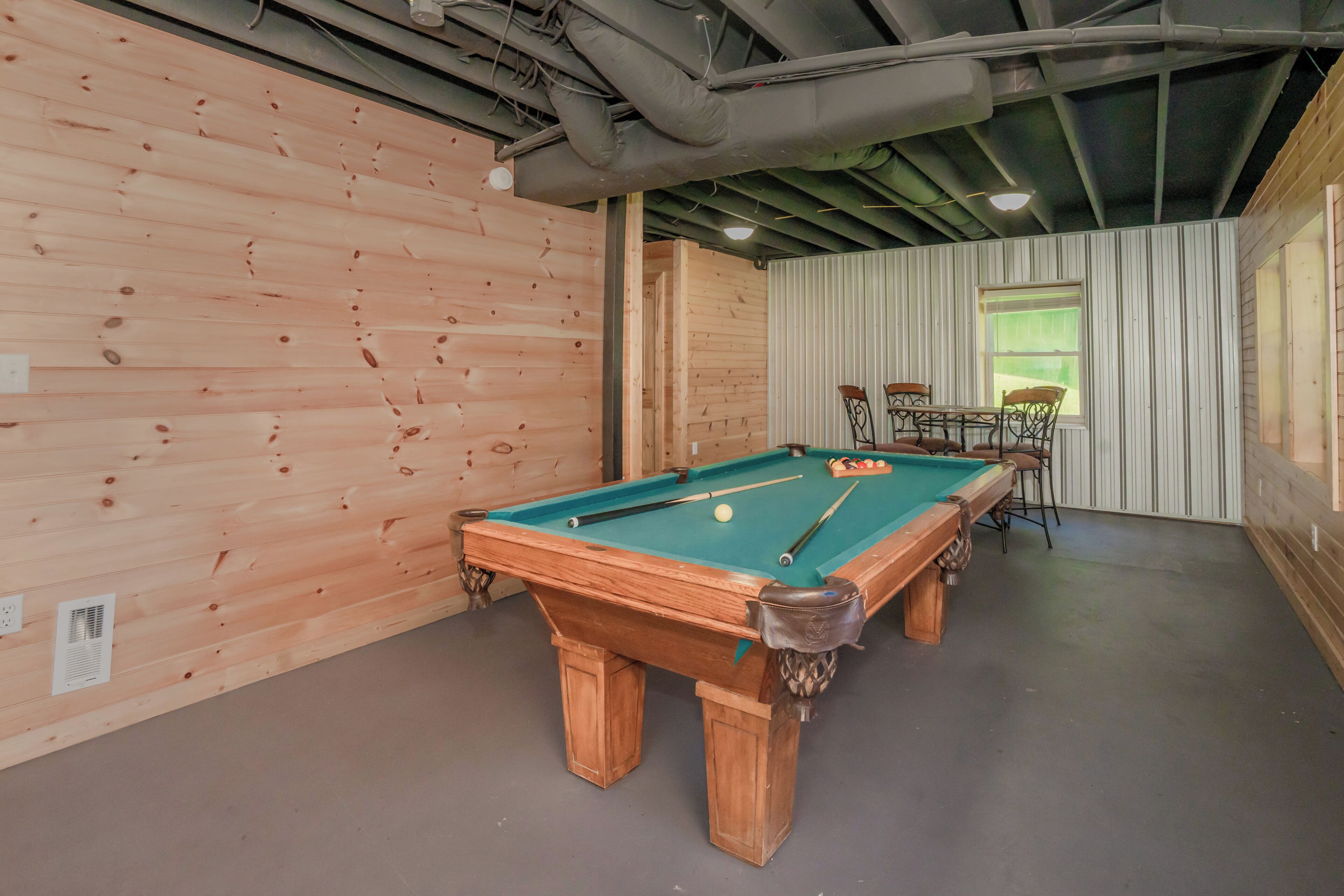 A pool table in a room with wooden walls and a window.