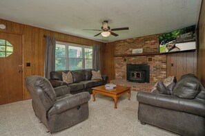 A living room with a fireplace, leather sofas, and a television. - 🌲 70 Acre Mountain Farmstead 🏞️ Stocked Pond, Game Room & Seclusion (Sevierville)