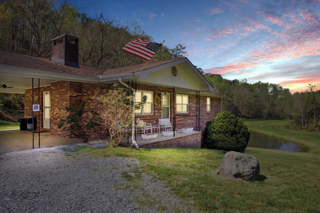 A brick house with a porch, a flag, and a pond.
