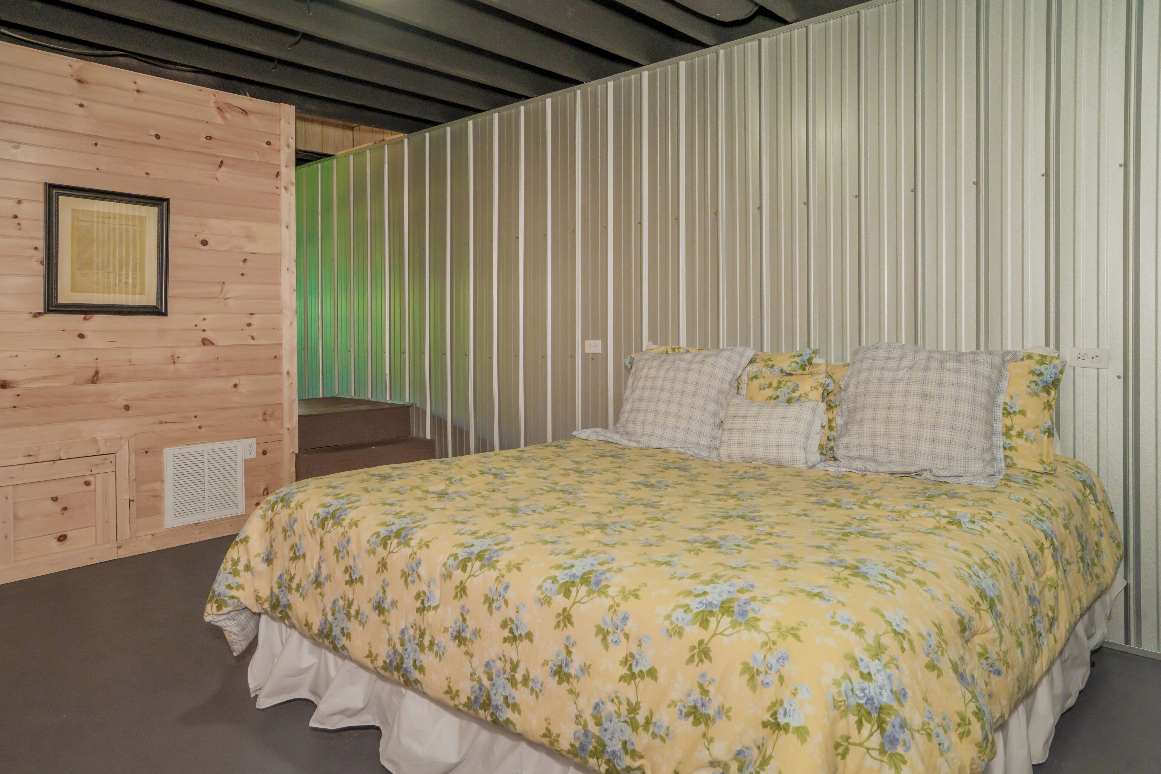 A room with a bed, a framed certificate on the wall, and a vent on the left.