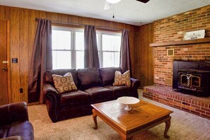 Una sala de estar con sofá de cuero, una mesa de centro de madera, chimenea y una ventana con cortinas.