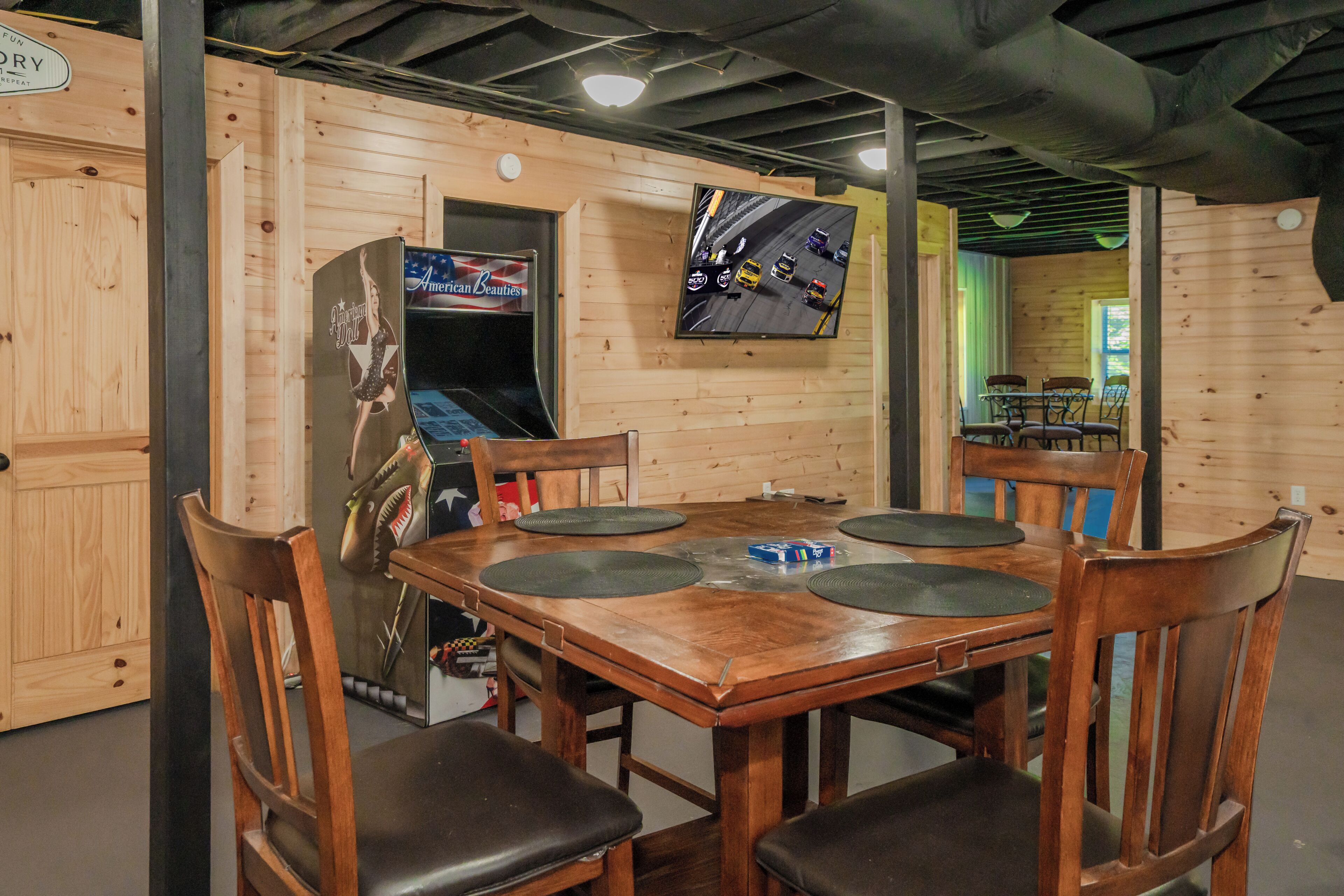 A wooden interior with a table and chairs, a television mounted on the wall, and a sign on the door.