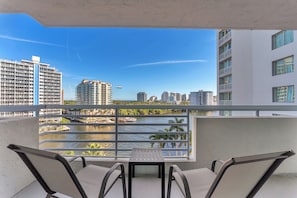 A balcony with a table and chairs, overlooking a river with buildings and a boat in the distance. - Atlantic Ocean Sunrise Suite Unit 820 (Fort Lauderdale)