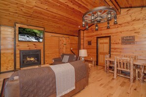 Ein rustikales Holzhaus-Interieur mit Kamin, einer Couch, einem Fernseher und einem Essbereich.