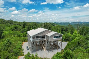 Eine zweistöckige Hütte mit Balkon und einer Treppe, die zum Obergeschoss führt, umgeben von dichtem Wald.