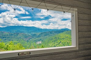 Ein Fenster mit Blick auf eine gebirgige Landschaft, ein Rauchverbot-Schild und Lichterketten.