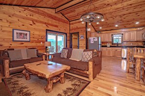 Ein Interieur einer Holzhütte mit Holzbalkendecke, einer Couch, einem Couchtisch und einer Küchenzeile.