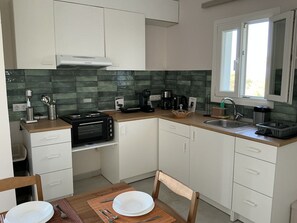 A compact kitchen with white cabinets, a built-in oven, a coffee maker, and a window. - Elaia Pearl Apartment with Sea, Dune & Lake Views, Wi-Fi and Air Conditioning (Linia)