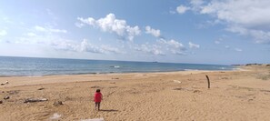 A beach with a person walking on the sand, the ocean, and a clear sky.