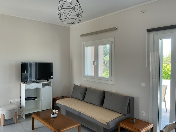 A modern living room with a sofa, a TV, a desk, and a dining table. - Elaia Pearl Apartment with Sea, Dune & Lake Views, Wi-Fi and Air Conditioning (Linia)