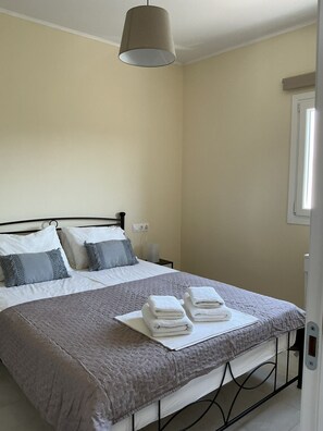 A neatly made bed with a grey quilt, white pillows, and a grey throw blanket. There are folded white towels on the bed. - Elaia Pearl Apartment with Sea, Dune & Lake Views, Wi-Fi and Air Conditioning (Linia)