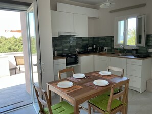 A modern kitchen with white cabinets, a microwave, stove, and a sink. There is a dining table with chairs and a view of greenery outside.