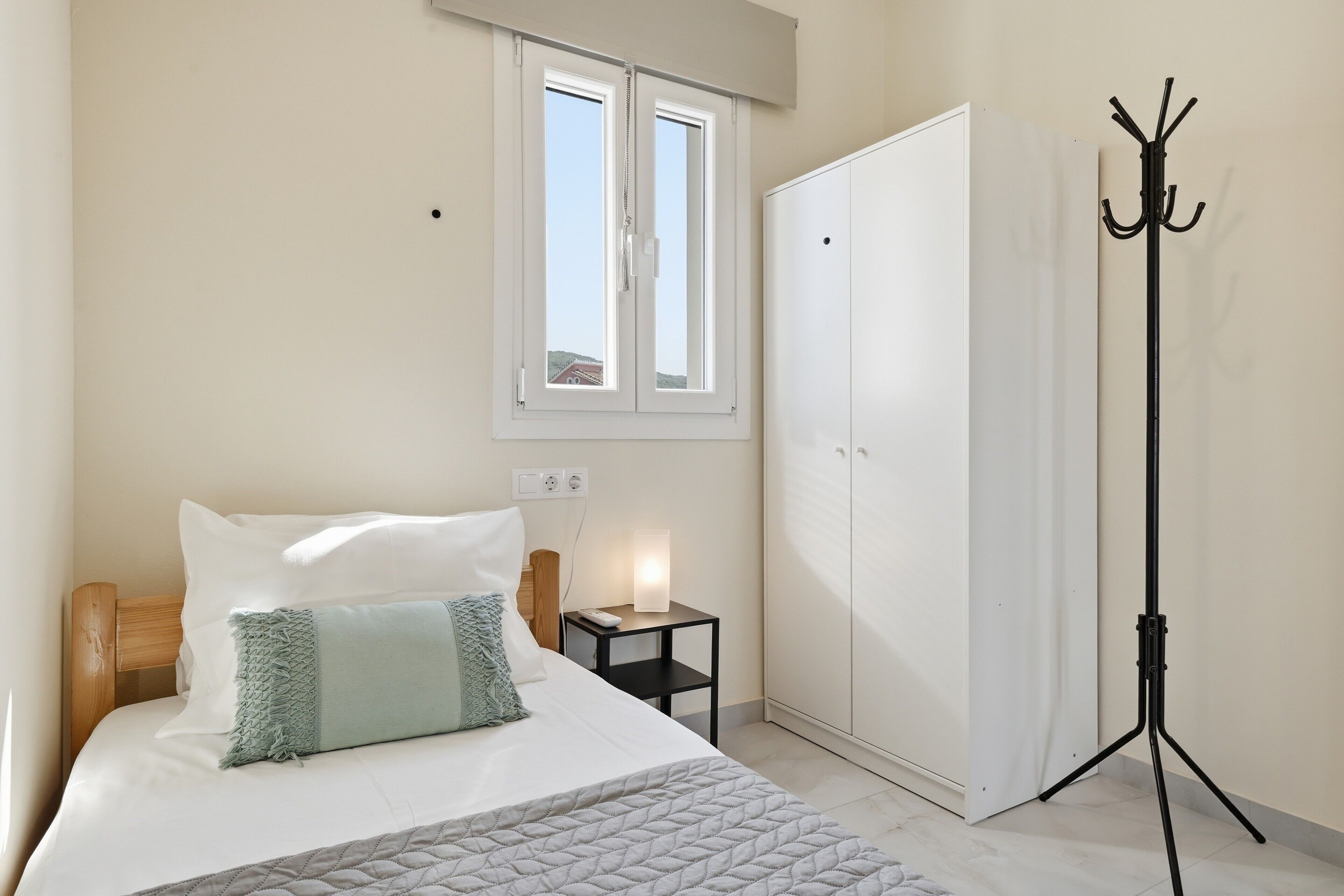 Une chambre à coucher comprenant un lit, une table de chevet, une lampe, une armoire et un porte-manteau.