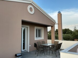 A balcony with a table and chairs, a door, and a chimney.