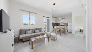 A modern living room with a sofa, coffee table, and TV, connected to a kitchen with a dining area.