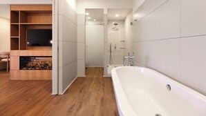 A modern bathroom with a bathtub, shower, and a built-in TV shelf.