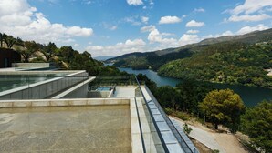 Ein modernes Gebäude mit Glasfassade, das auf einen Fluss und Hügel blickt.