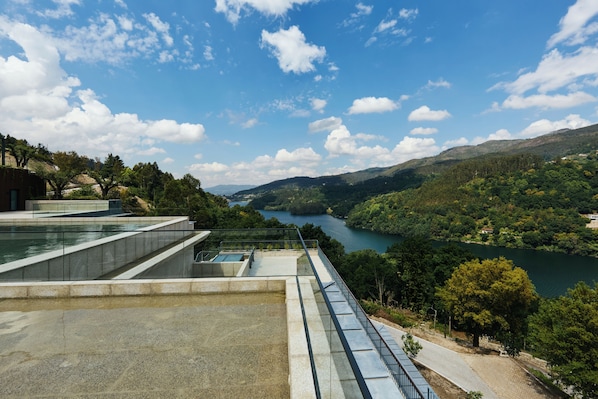 A modern building with a glass facade overlooking a river and hills.