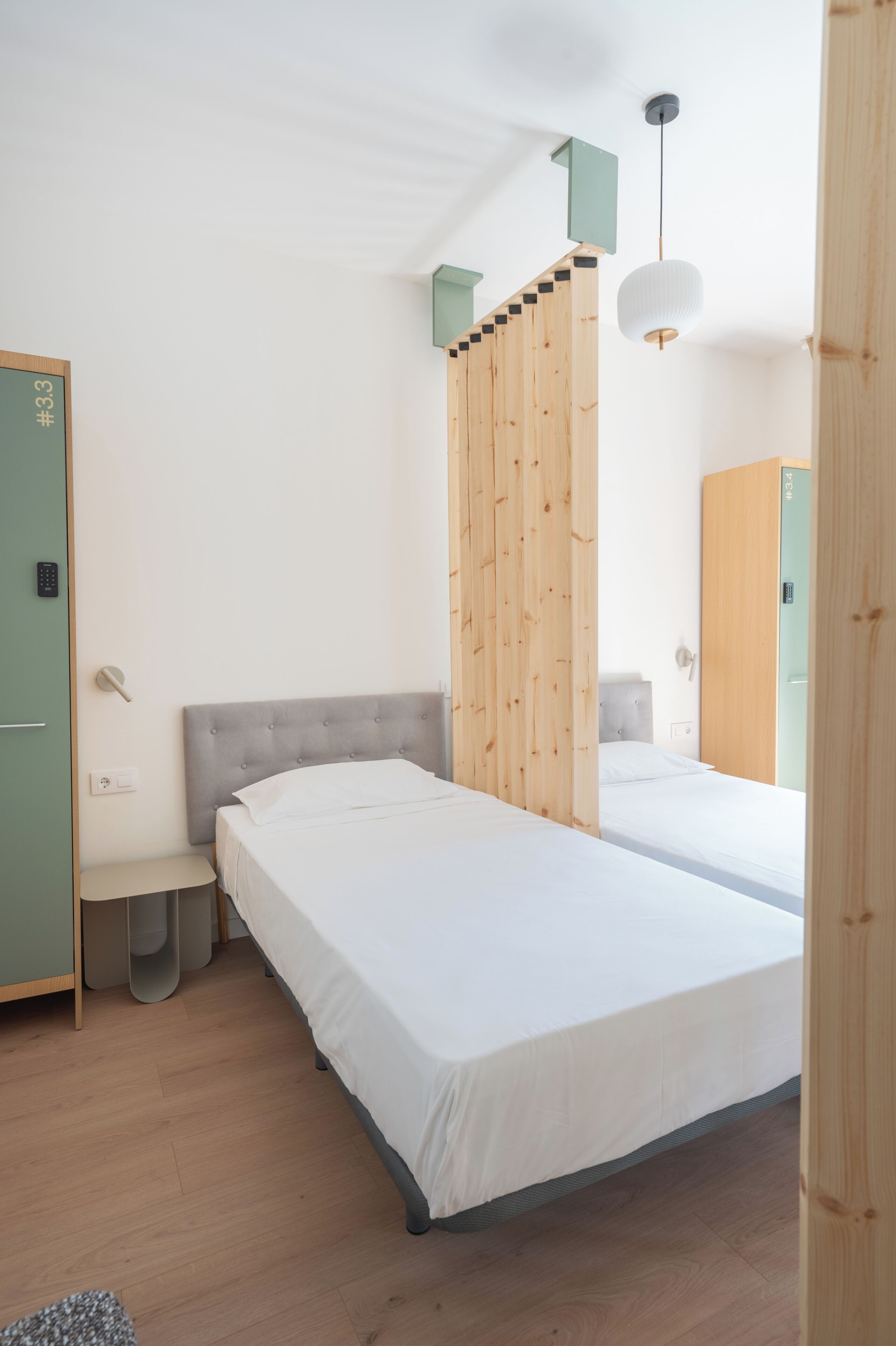 Un dormitorio moderno con dos camas, un separador de madera, un pequeño banco y un armario.