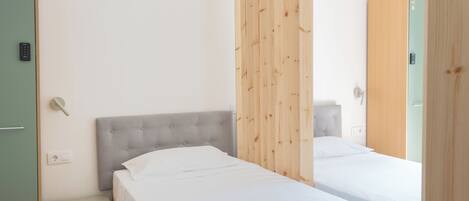 Un dormitorio moderno con dos camas, un separador de madera, un pequeño banco y un armario.