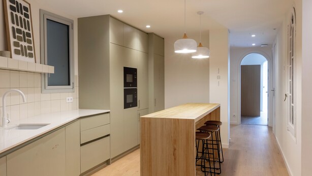 A modern kitchen with a central island, bar stools, recessed lighting, and a view into the dining area. - Casa Nido Diagonal (Barcelona)
