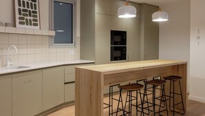 A modern kitchen with a wooden island, bar stools, recessed lighting, and a window. - Casa Nido Diagonal (Barcelona)