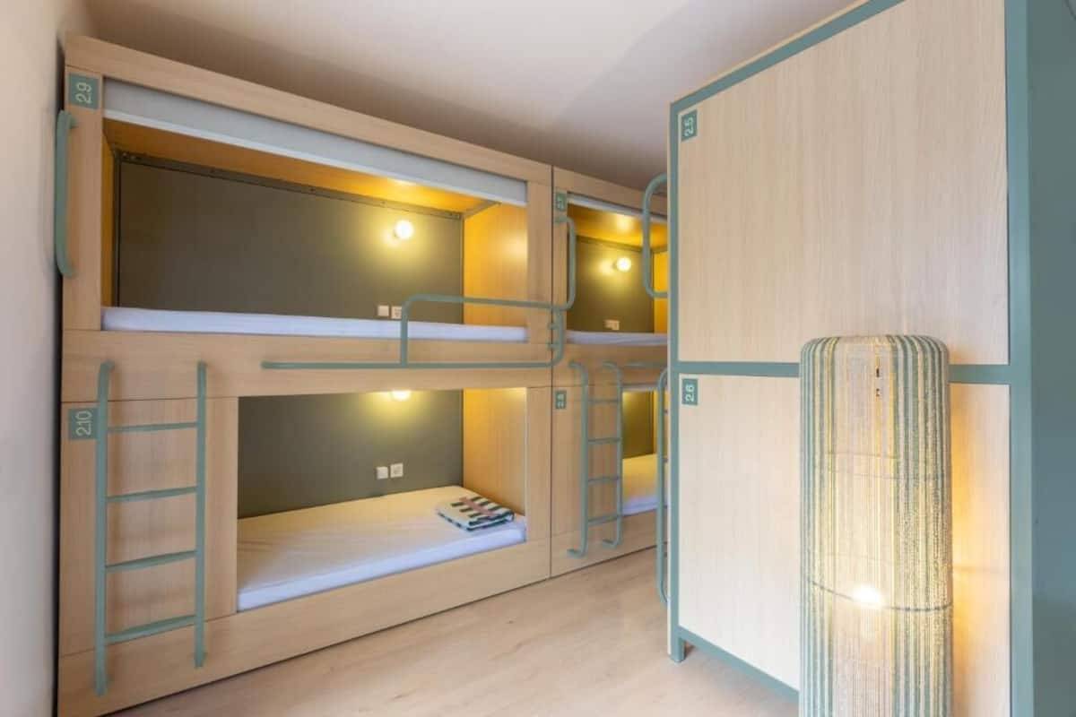 Habitación con literas, una mesita pequeña y una lámpara fijada en la pared.