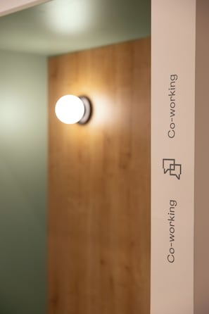 A wooden door with a circular light fixture and a vertical sign with the text 'Co-working.' - Casa Nido Diagonal (Barcelona)