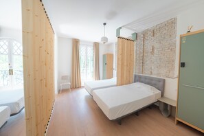 A room with two beds, a wooden wardrobe, a green door, and a brick wall. - Casa Nido Diagonal (Barcelona)