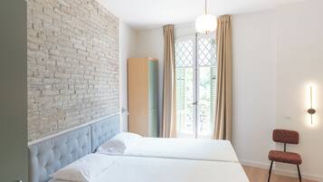 A modern bedroom with a bed, a wardrobe, a chair, and a brick wall.