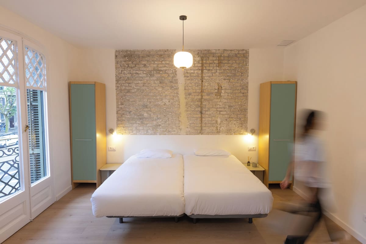Un dormitorio con una cama doble, dos mesitas de noche, una lámpara colgante y una pared de ladrillo.