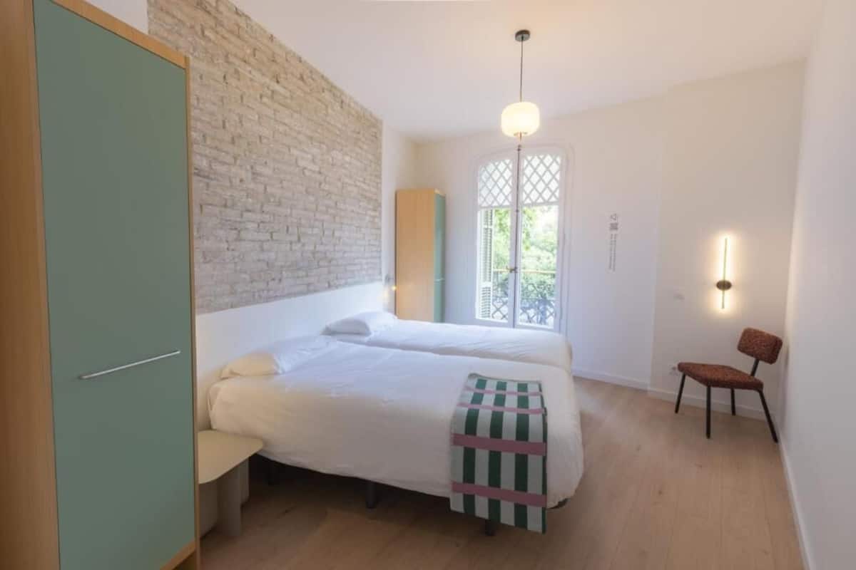 Un dormitorio con cama, una silla, armario y ventana con vistas.