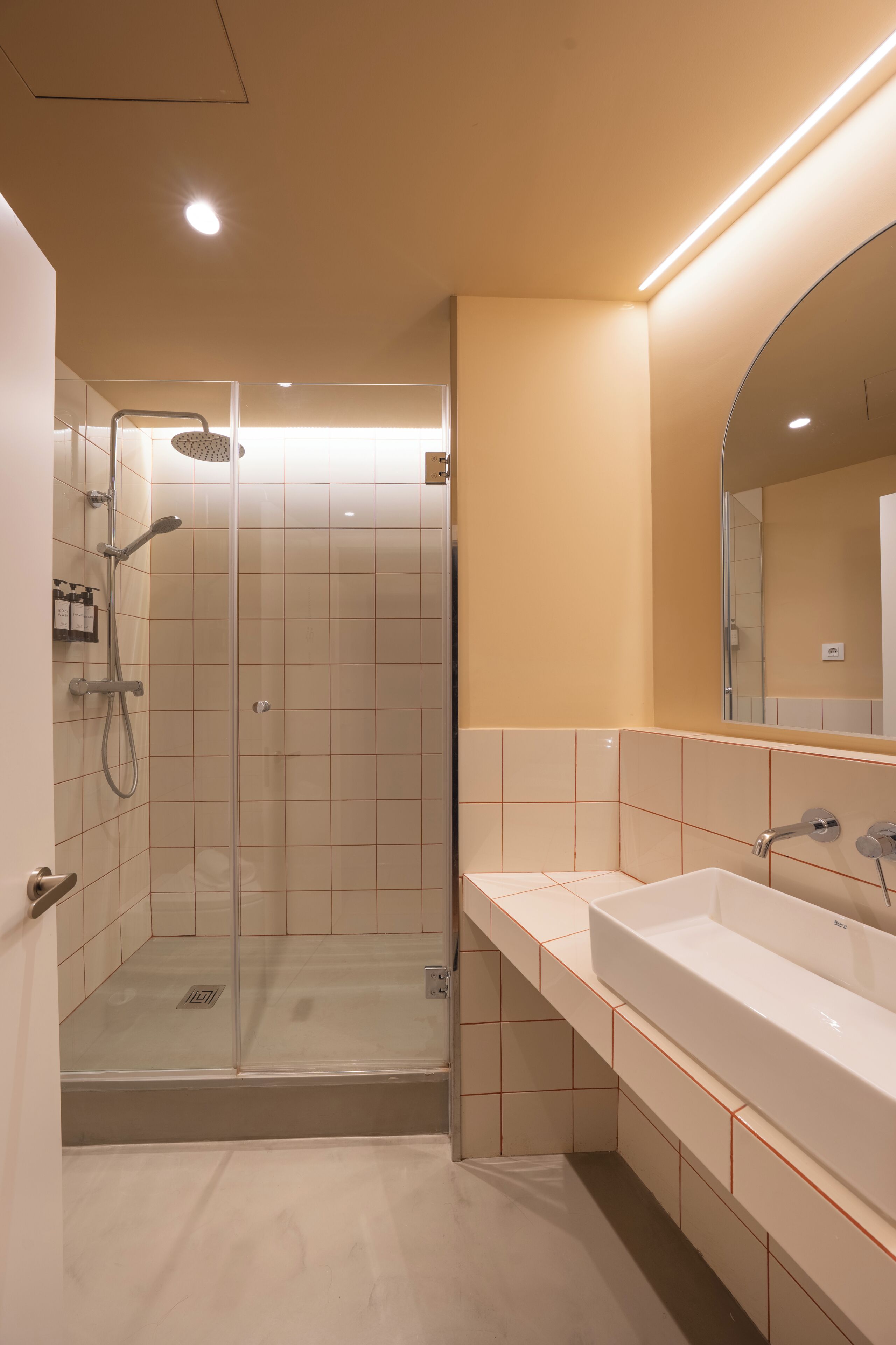 A modern bathroom with a glass-enclosed shower, a large mirror, and a white sink.